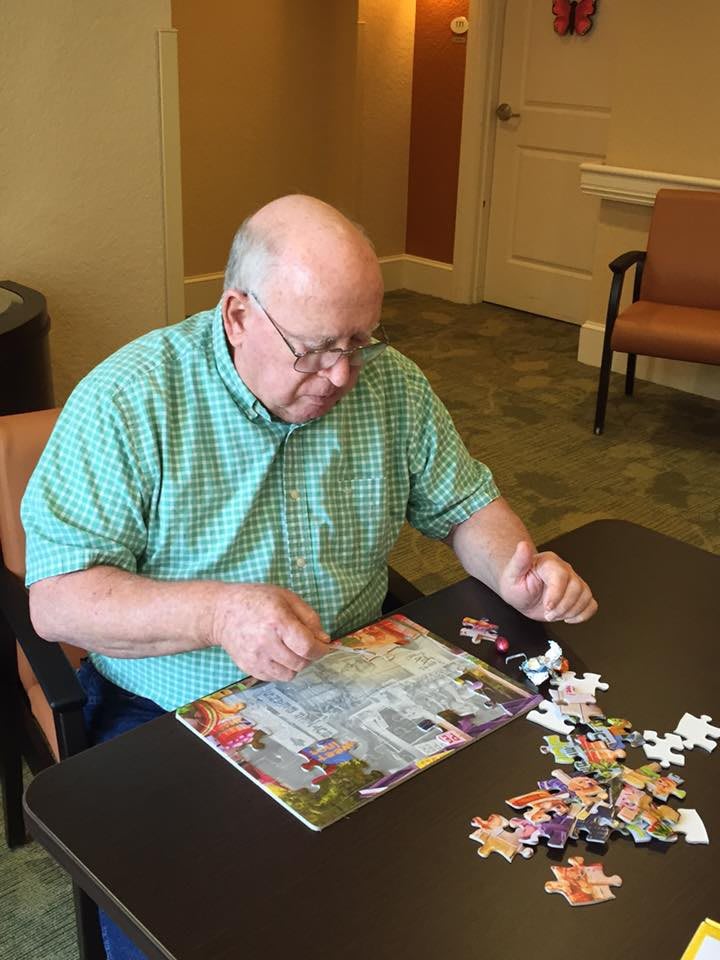 An elderly man working on a jigsaw puzzle at a table indoors.