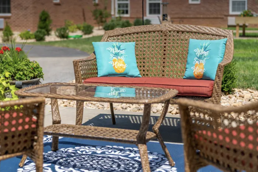 A cozy outdoor seating area featuring a wicker sofa with colorful cushions and a glass-top coffee table, perfect for relaxation.