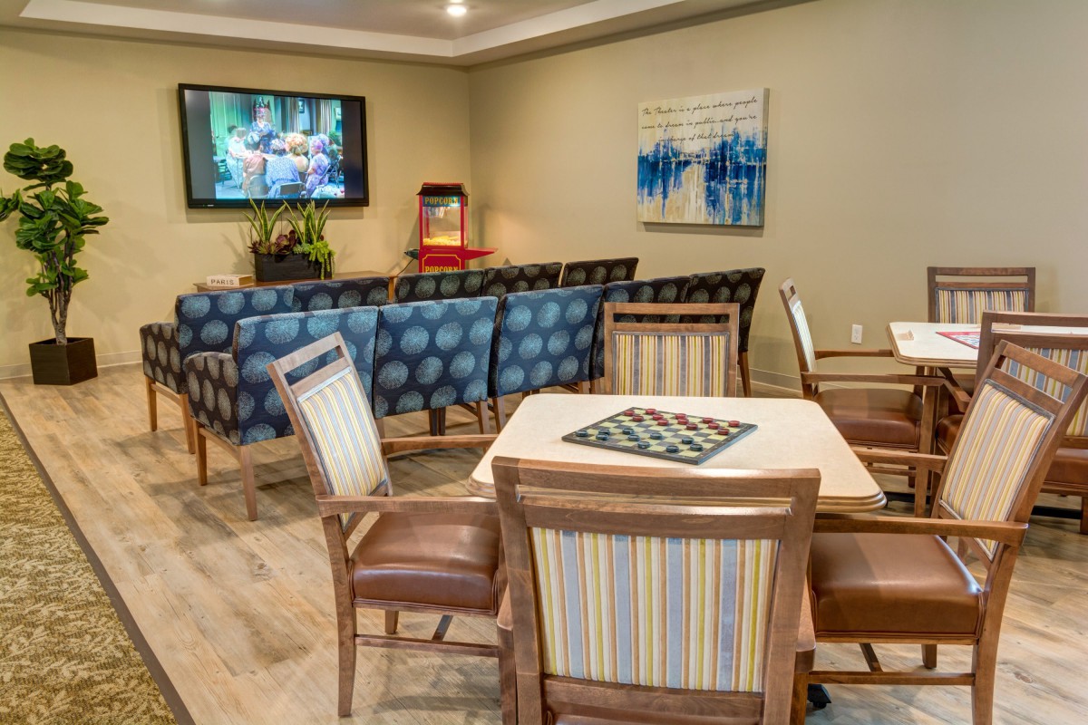 A cozy seating area with a television, artwork on the walls, and comfortable chairs arranged around a table.
