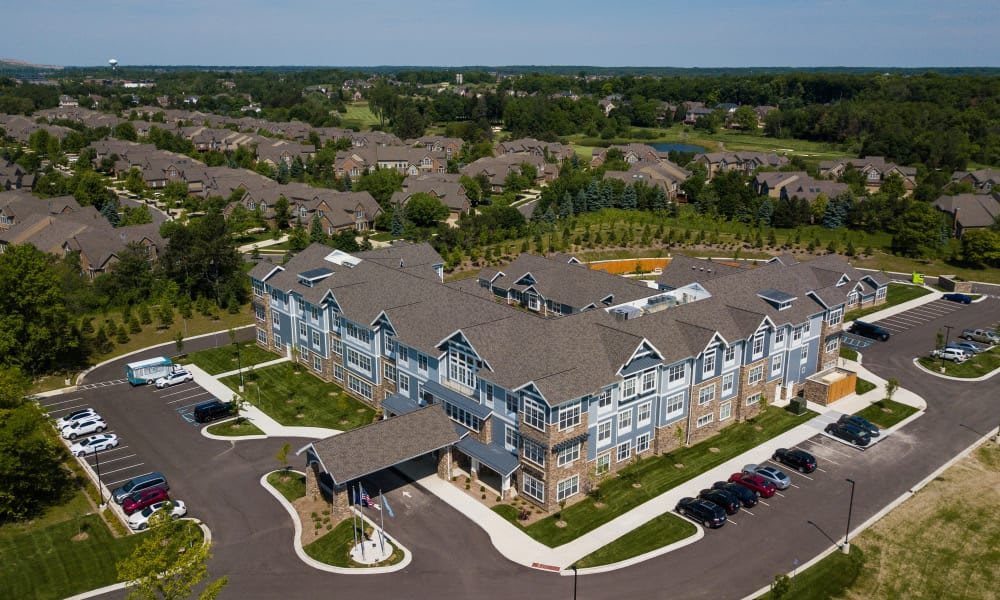 Aerial view of a large, multi-story residential building with landscaped surroundings and a parking lot in a suburban area.