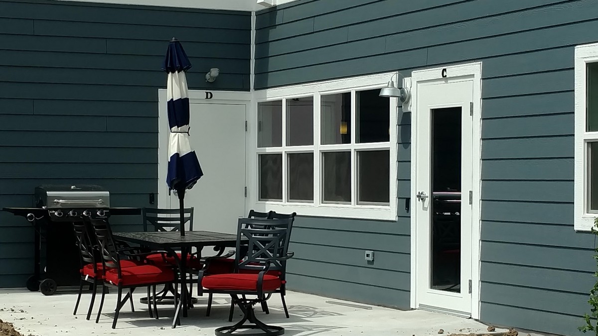 An outdoor patio with a table, chairs, and an umbrella next to the exterior of a house.