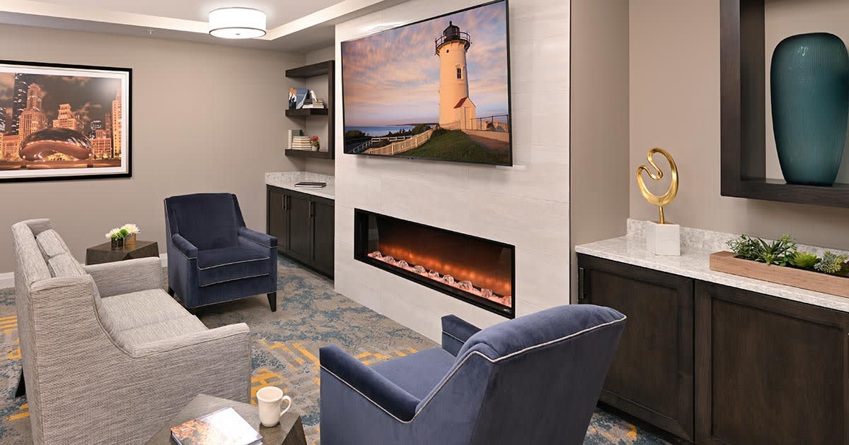 A cozy living room featuring a modern fireplace, comfortable seating, and a flat-screen TV displaying a lighthouse scene.