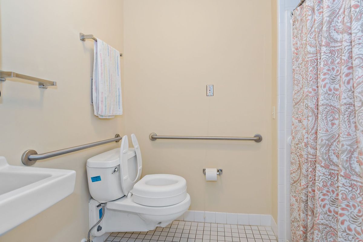 A clean and accessible bathroom with a toilet, sink, towel, and grab bars.