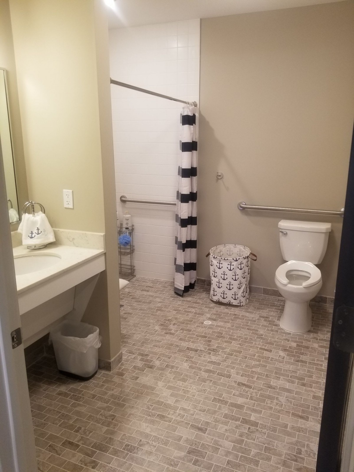 A clean and spacious bathroom with a toilet, sink, and shower area featuring a striped curtain.