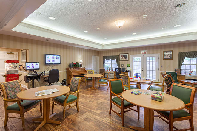A cozy community room with tables, chairs, a computer station, and a piano.