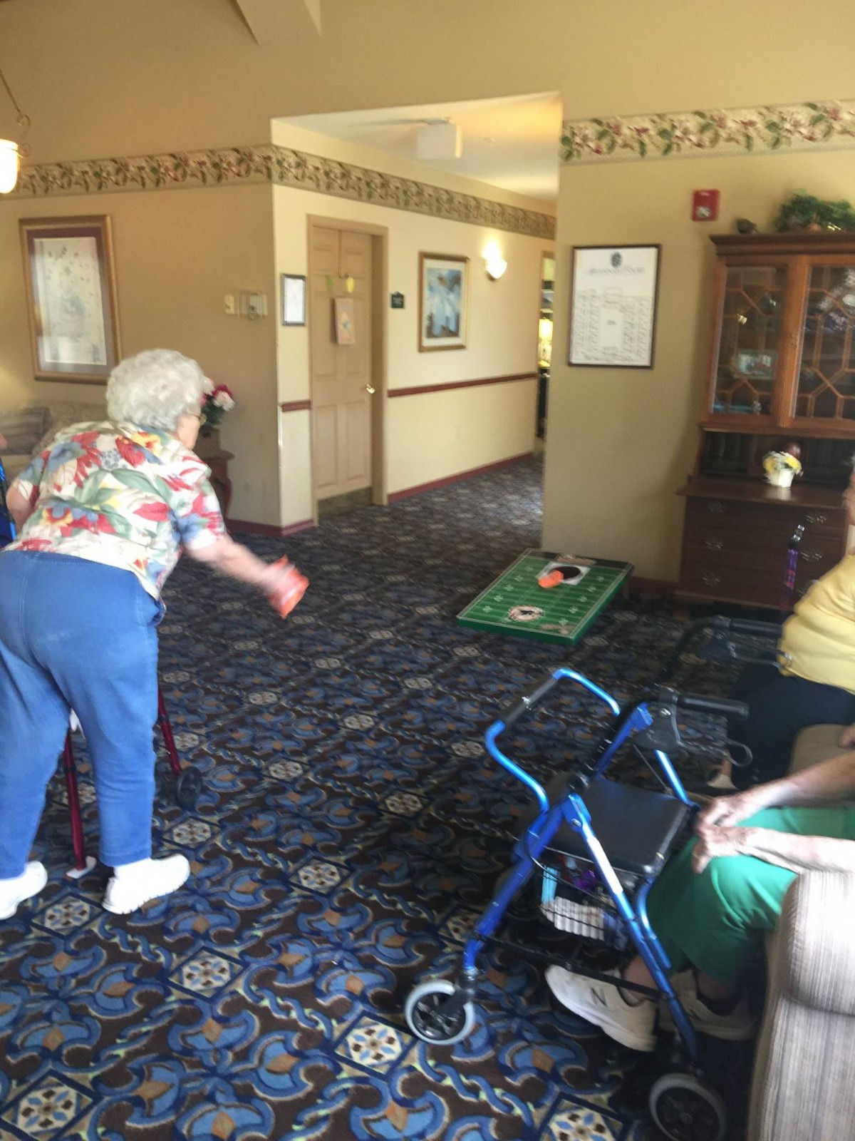 Elderly individuals enjoying a game of cornhole in a common area.