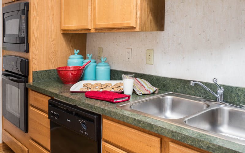 A kitchen countertop with cookies on a tray, surrounded by colorful canisters and a sink.