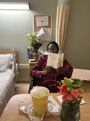 A patient enjoying a book surrounded by flowers in a hospital room.