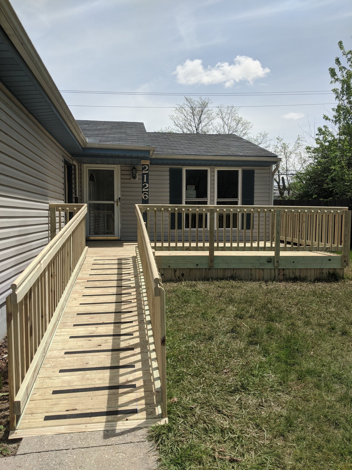 A house with a wooden deck and an accessibility ramp leading to the backyard.