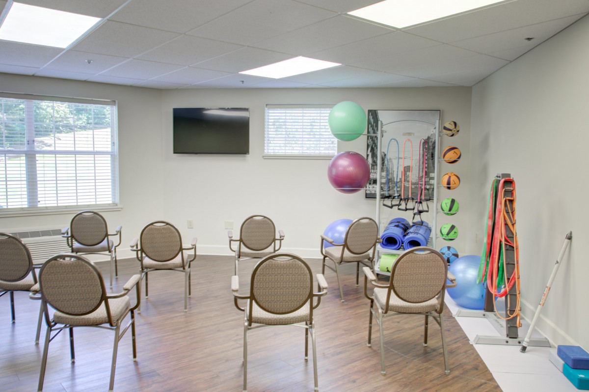 An exercise room with chairs arranged in rows, fitness equipment including yoga balls and mats, and a television mounted on the wall.