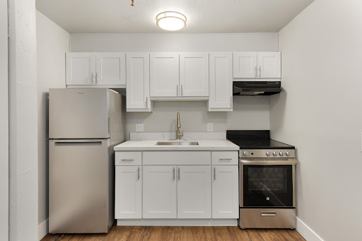 A modern kitchen featuring white cabinets, stainless steel appliances, and a warm hardwood floor.