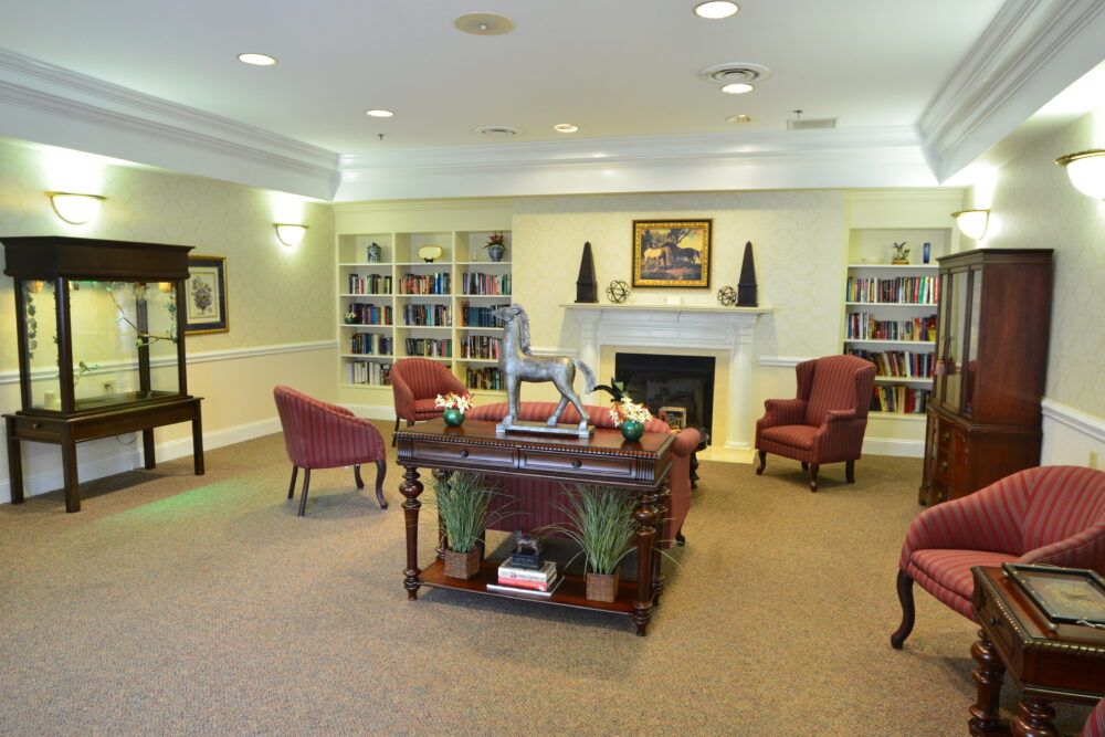 A cozy library interior with bookshelves, armchairs, and a central table by the fireplace.