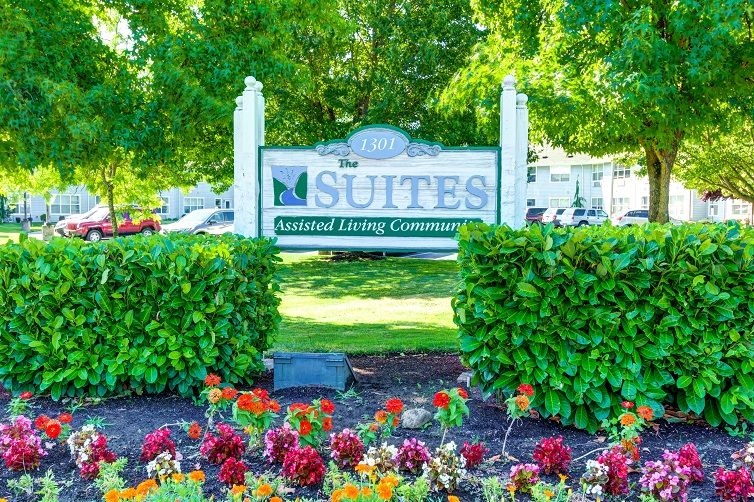 Entrance sign for a suites living community surrounded by flowers and greenery.