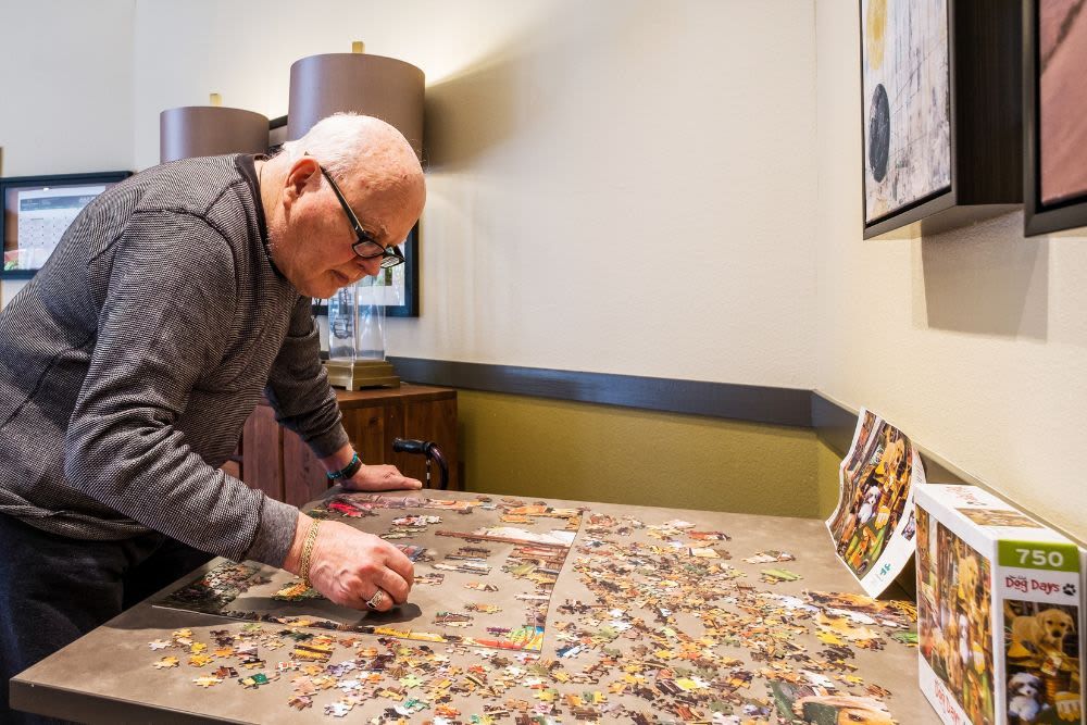 An elderly man working on a jigsaw puzzle at a table indoors.