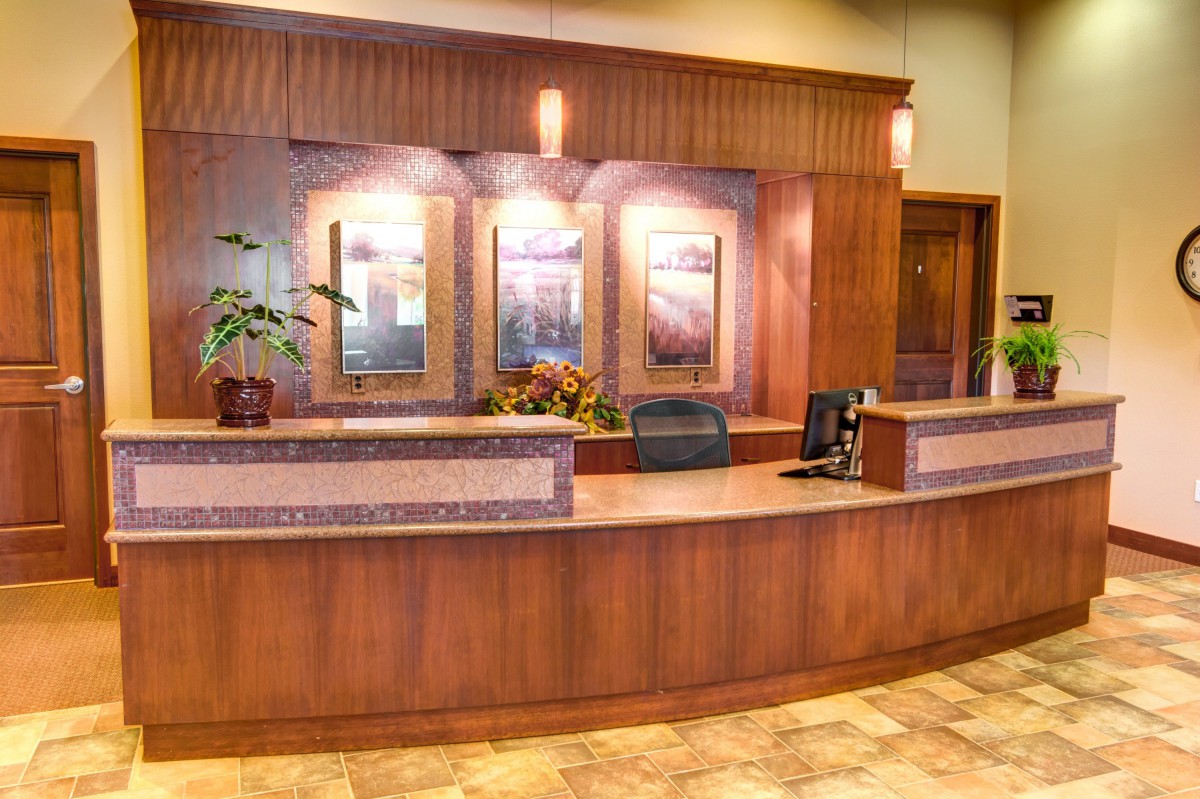 A well-lit reception area with a wooden front desk and decorative plants.