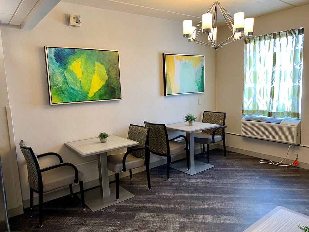 A small dining area with modern artwork, featuring two tables and several chairs under a contemporary chandelier.