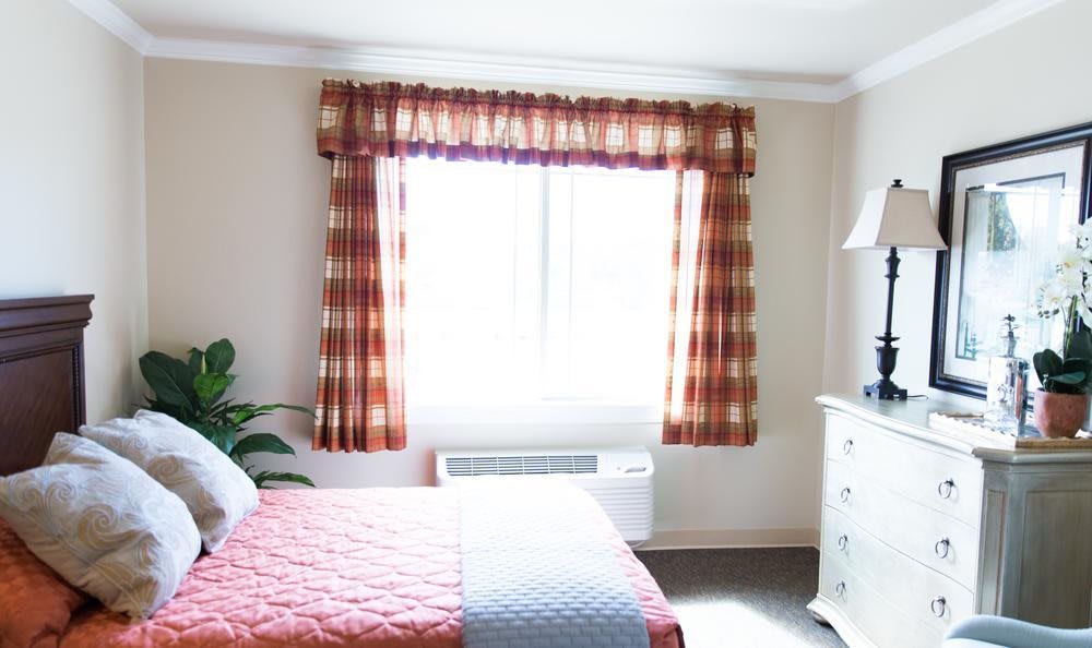 A bright bedroom with a window covered by plaid curtains, featuring a bed and a dresser.