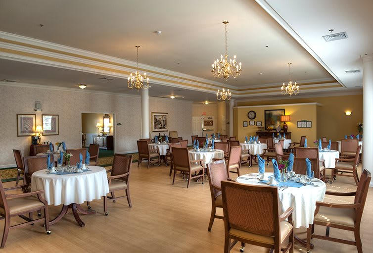 An elegant dining room with neatly arranged tables and chairs, set under glistening chandeliers.