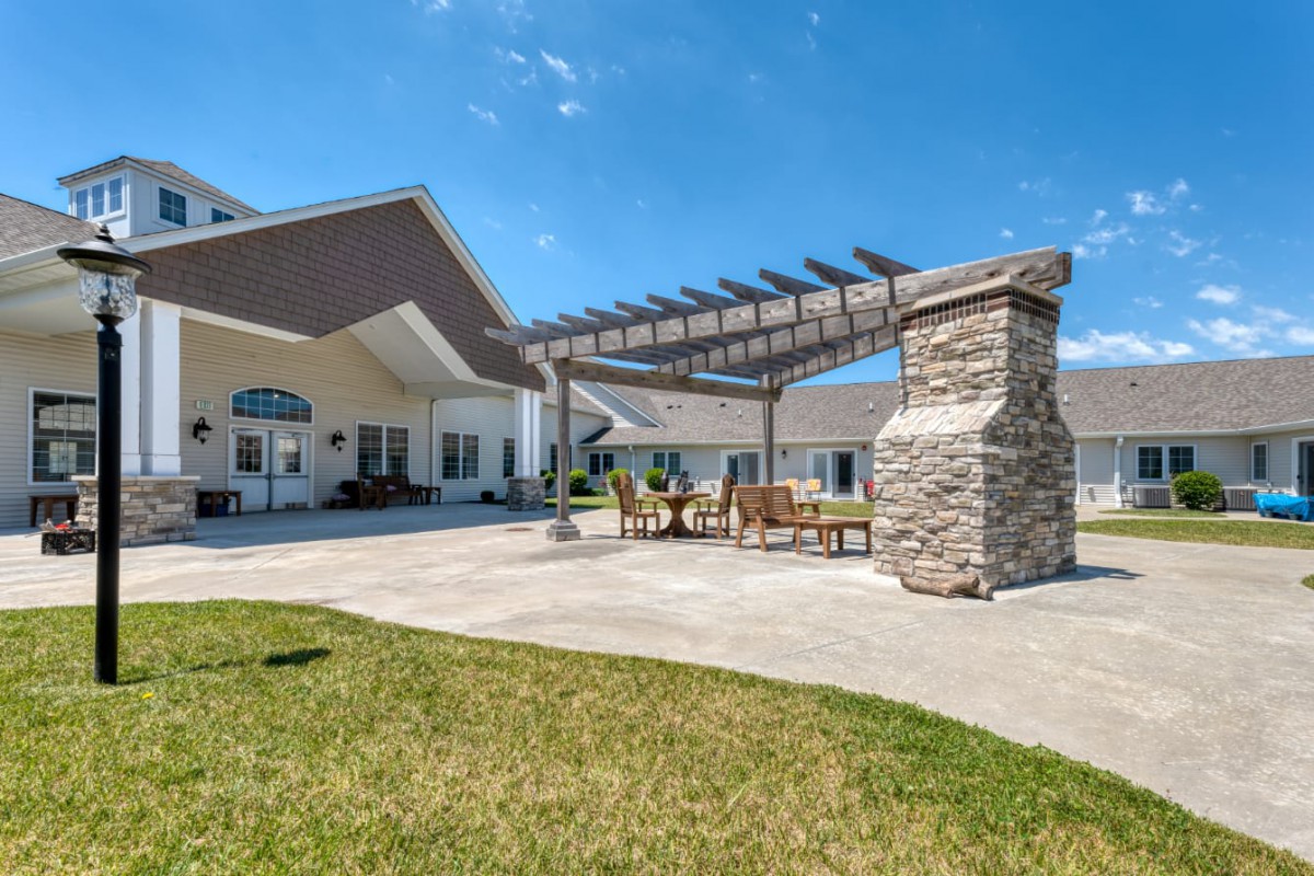 A sunny backyard patio featuring a pergola and stone fireplace.