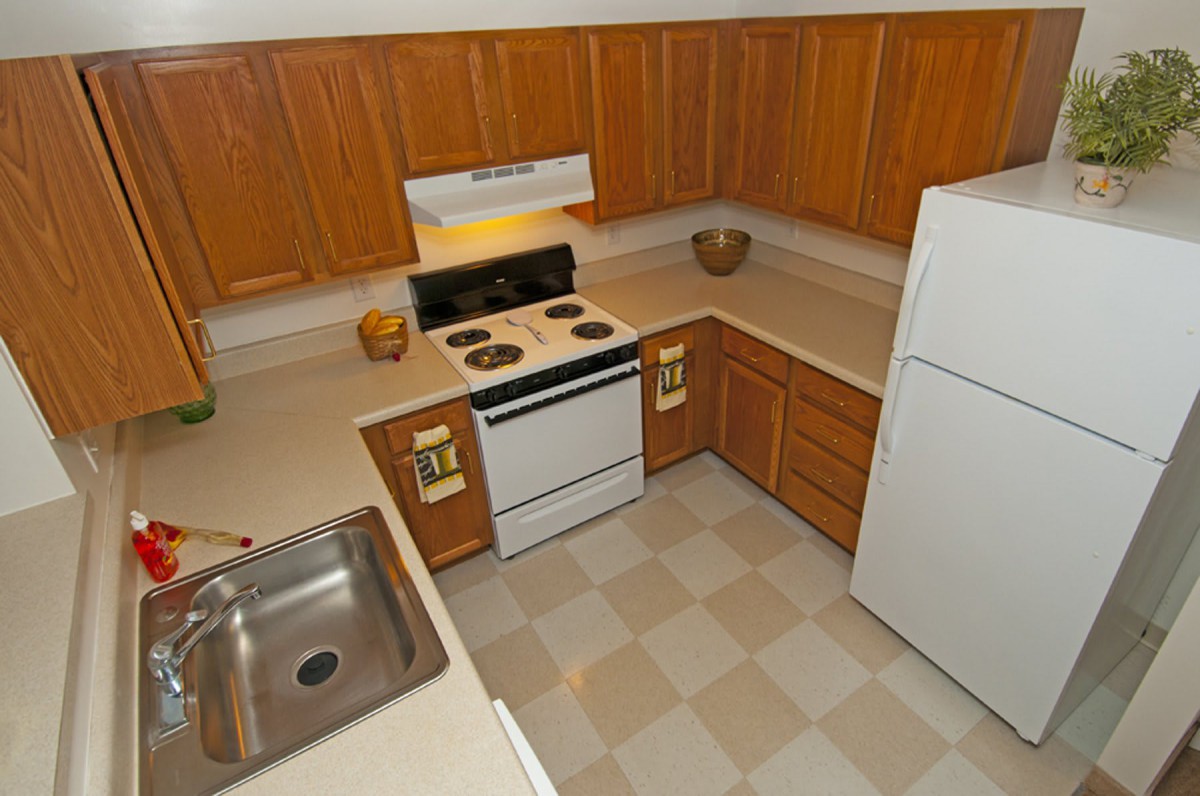 A clean and organized kitchen with wooden cabinets, a stove, sink, and refrigerator.
