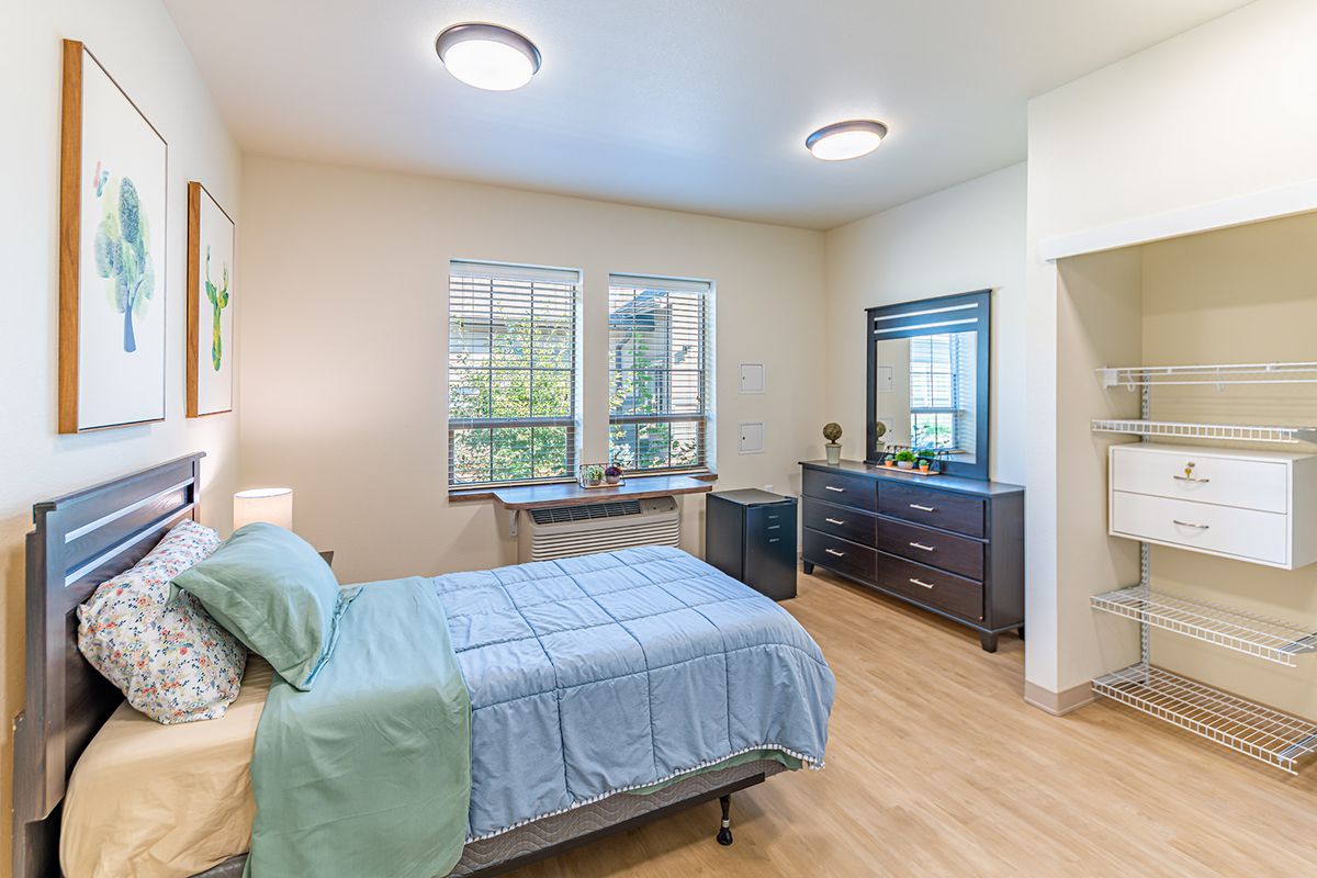 A modern bedroom with a minimalist design featuring a bed, dresser, and large windows.