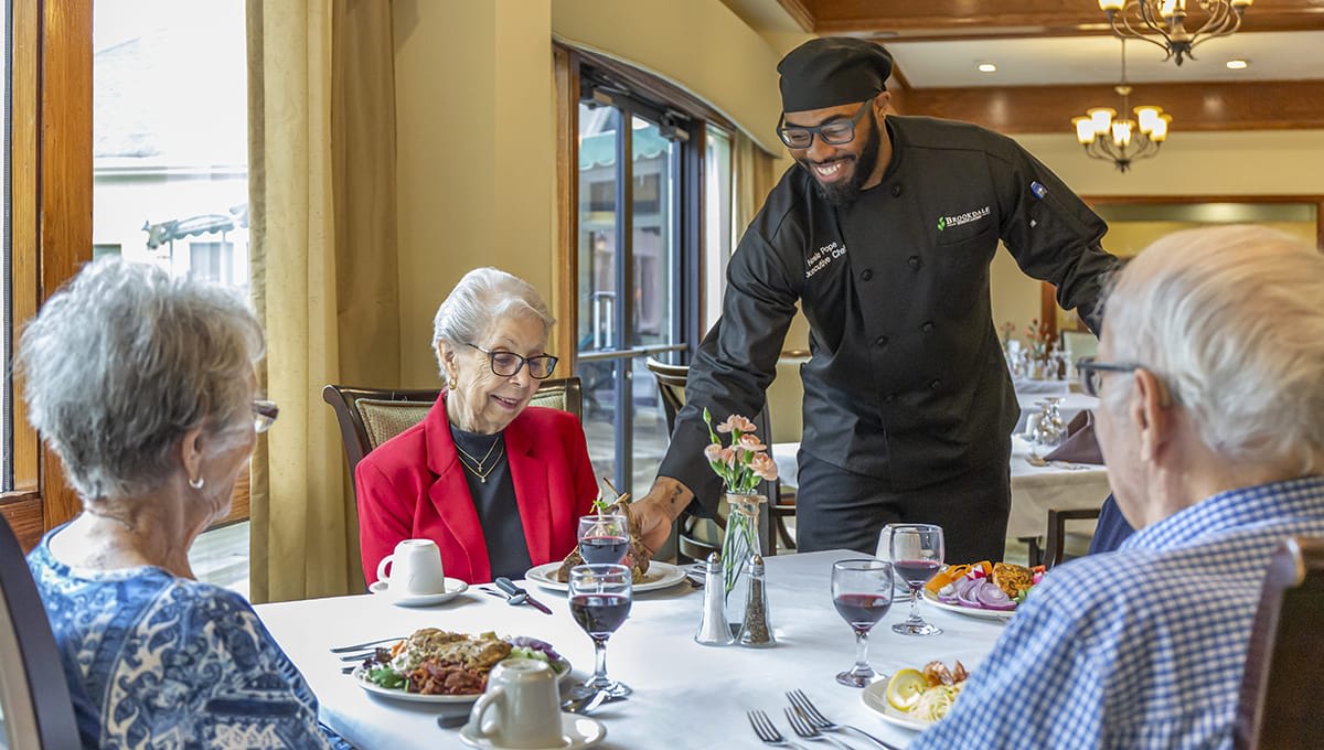 A server in a restaurant is attending to an elderly person enjoying a meal.