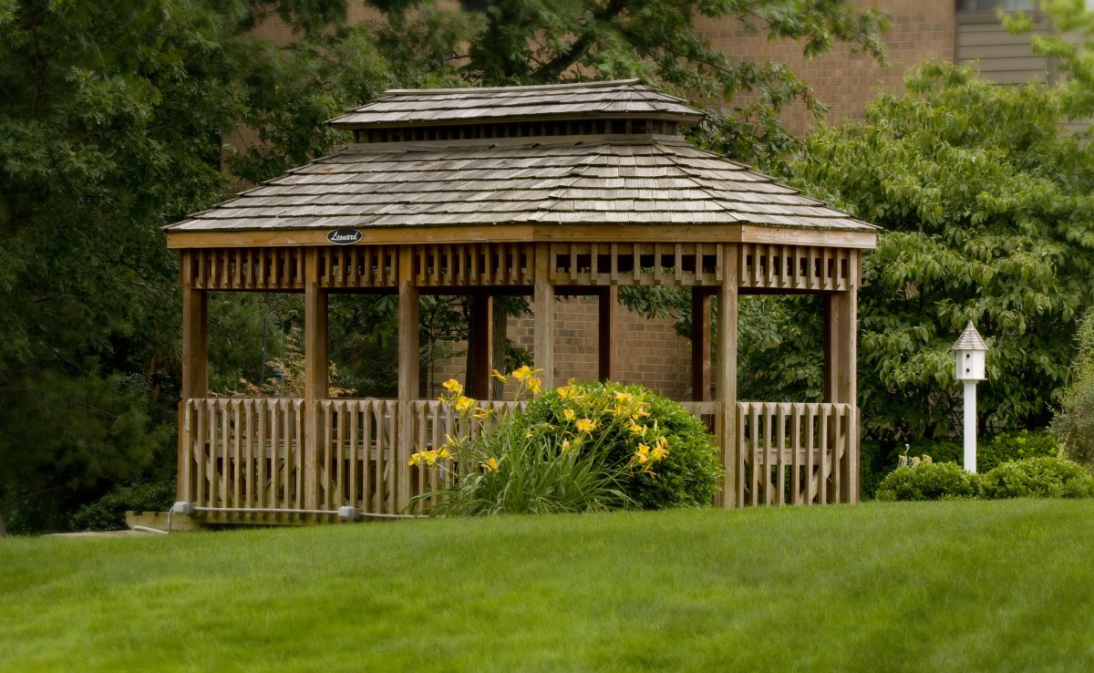 A quaint wooden gazebo surrounded by lush greenery and vibrant flowers.