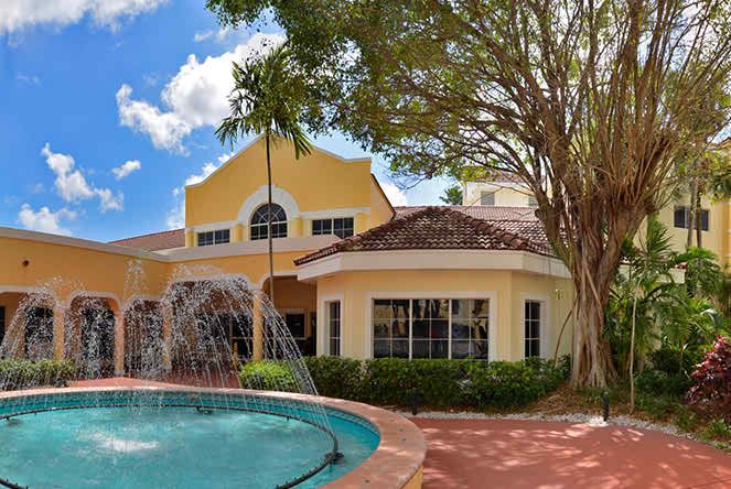 A yellow house with a pool and fountain in front, surrounded by trees.