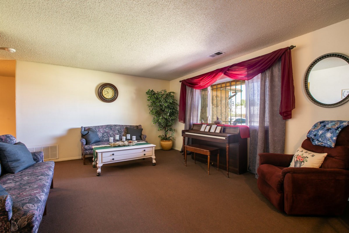 A cozy living room featuring a sofa, coffee table, and piano near a window with curtains.