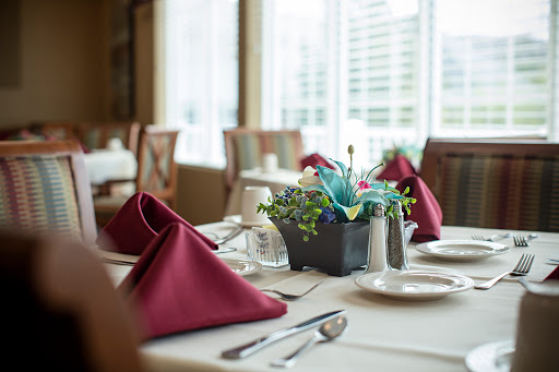 An elegantly set dining table featuring maroon napkins and a decorative floral centerpiece.