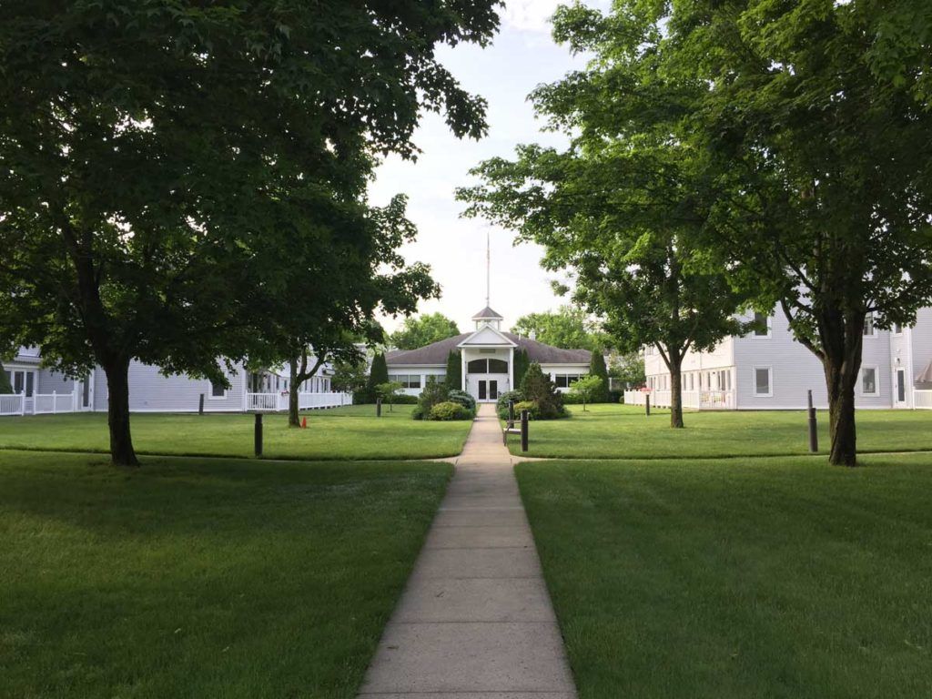 A picturesque view of a building surrounded by trees and a well-maintained lawn, with a pathway leading towards it.