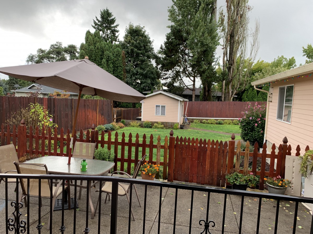 A cozy backyard with a patio set, umbrella, and fenced garden area on a cloudy day.