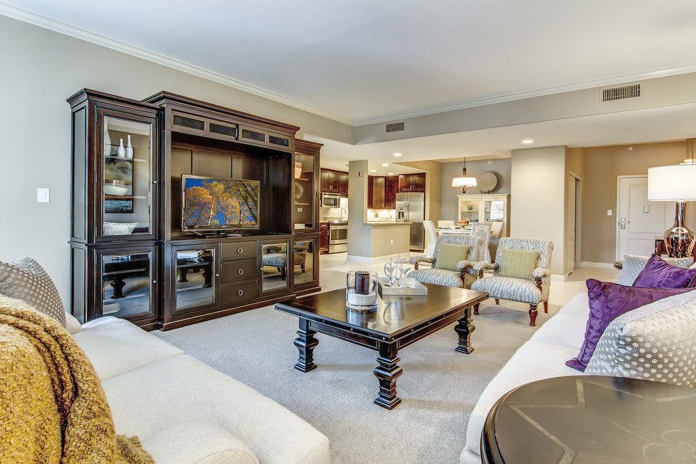 A spacious living room with elegant decor, featuring comfortable seating, a large entertainment unit with a television, and a central coffee table.