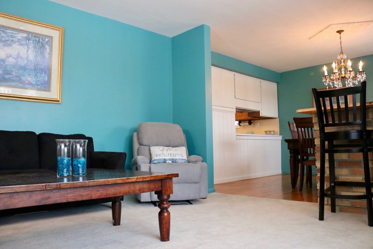 A cozy living room with blue walls, featuring a sofa and coffee table, adjacent to a kitchen and dining area.