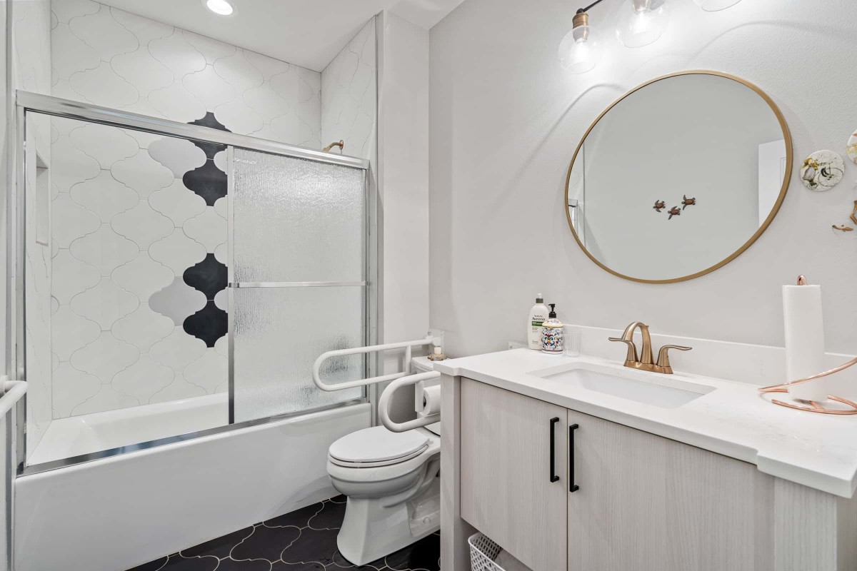 A modern bathroom with a large round mirror, white sink, and accessible features.
