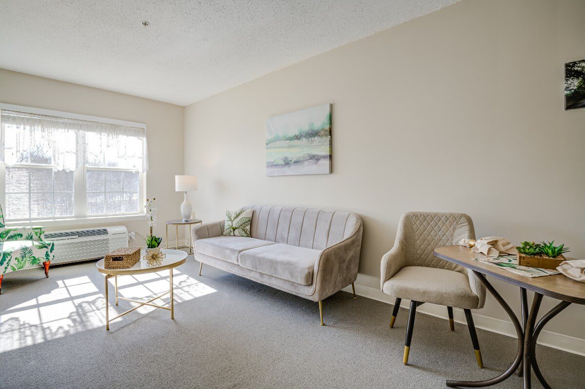 A bright and cozy living room with a sofa, chairs, coffee table, and artwork on the wall.
