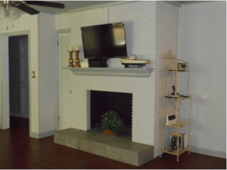 A modern living room features a flat-screen TV mounted above a fireplace, complemented by decorative items and a corner shelf.