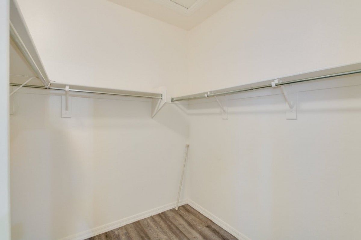 An empty walk-in closet with wooden flooring and shelving.