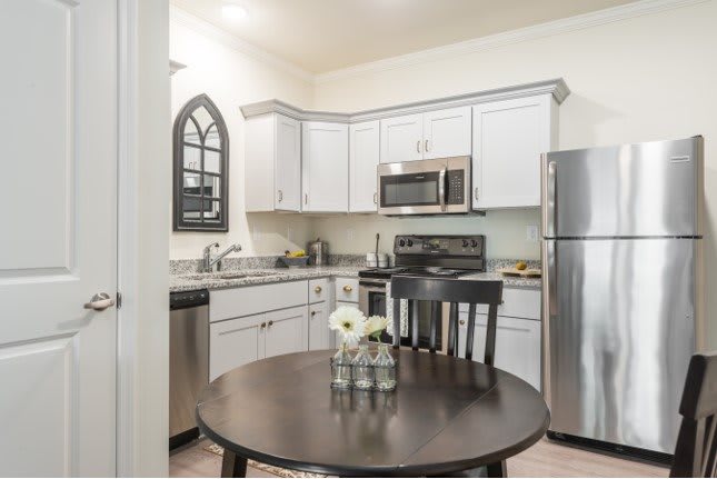 A modern kitchen with white cabinetry, stainless steel appliances, and a small dining table with a flower centerpiece.