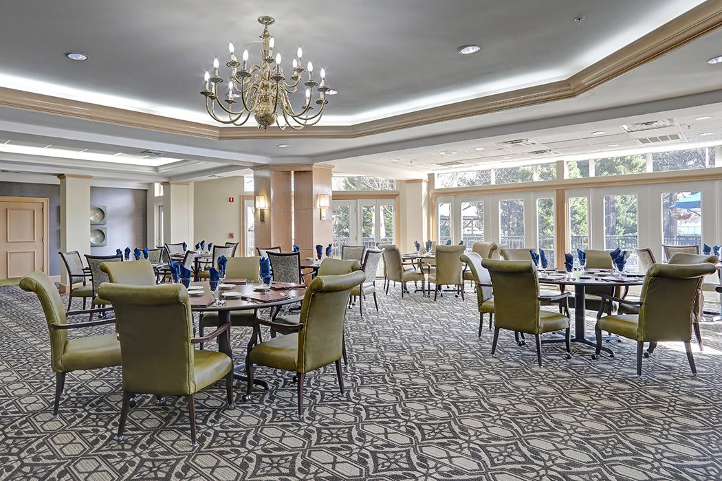 A spacious dining room with elegant chandeliers, tables, and chairs set on a carpeted floor.