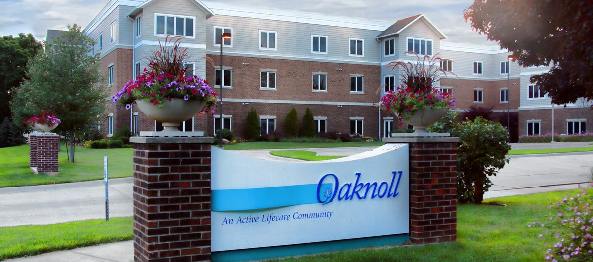 Sign for Oaknoll, an active retirement community, in front of a large brick building.