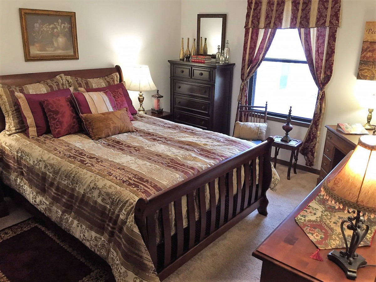 A cozy traditional bedroom with a wooden bed, dresser, and decorative pillows.