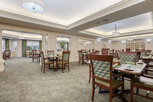A spacious and elegantly decorated dining room with multiple tables and chairs, featuring a carpeted floor and ambient lighting.