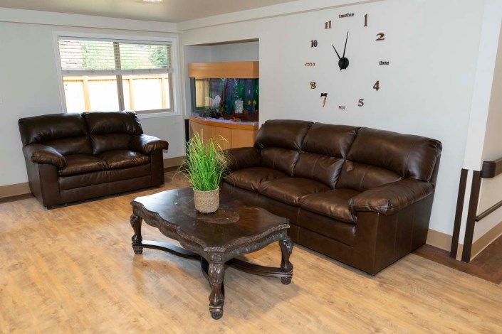 A cozy living room with leather sofas, a coffee table, and a large wall clock.