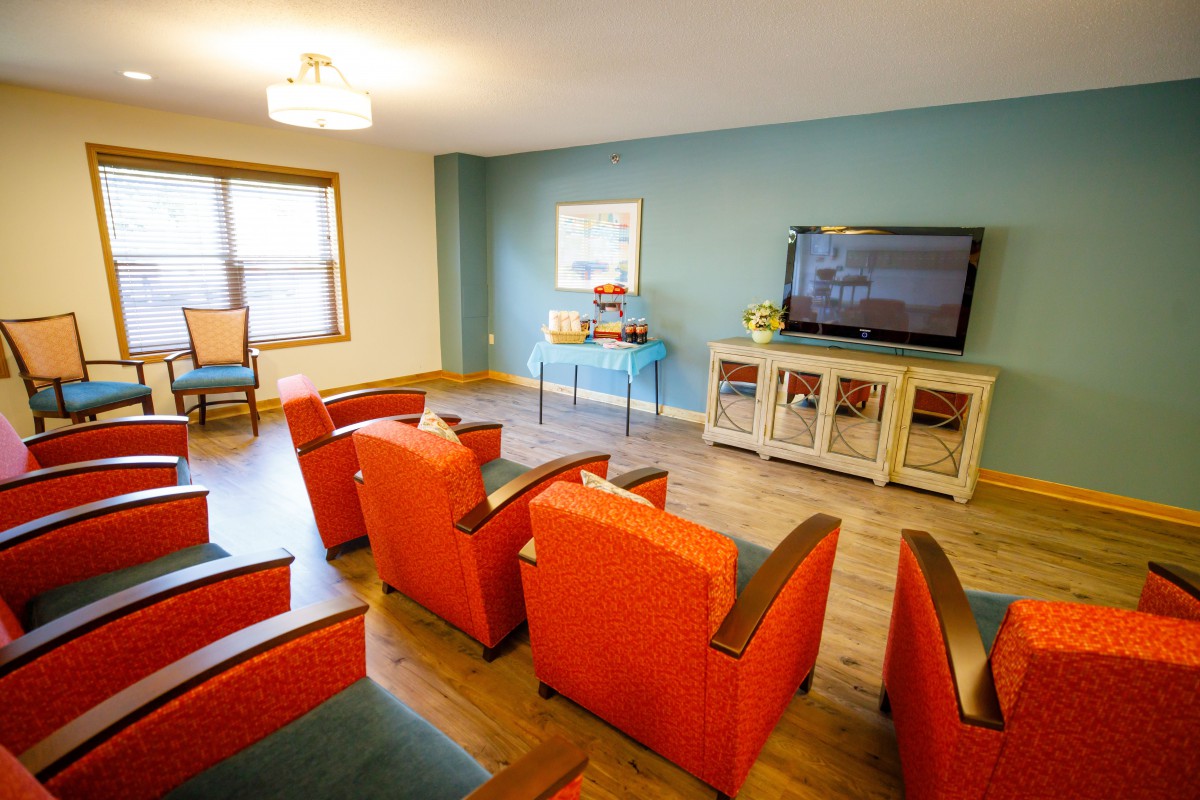 A vibrant living room with orange chairs and a wall-mounted TV.