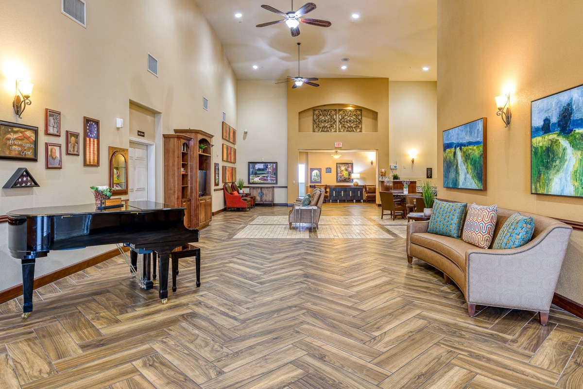 A spacious and elegantly decorated lobby featuring a grand piano, seating area, and artwork on the walls.