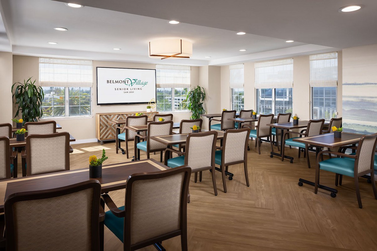 A modern conference room set up with tables and chairs, featuring a large presentation screen and bright lighting.