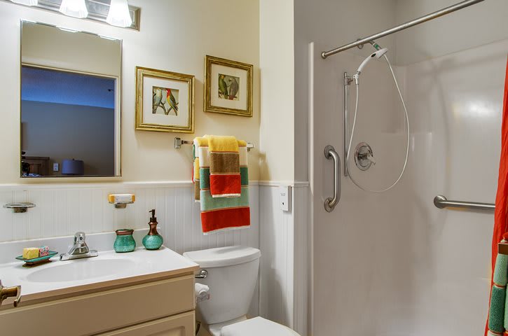 A cozy bathroom featuring a shower, sink, and colorful towels with decorative wall art.