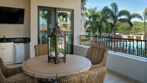 A serene balcony setting with wicker furniture and a decorative lantern, surrounded by lush palm trees.