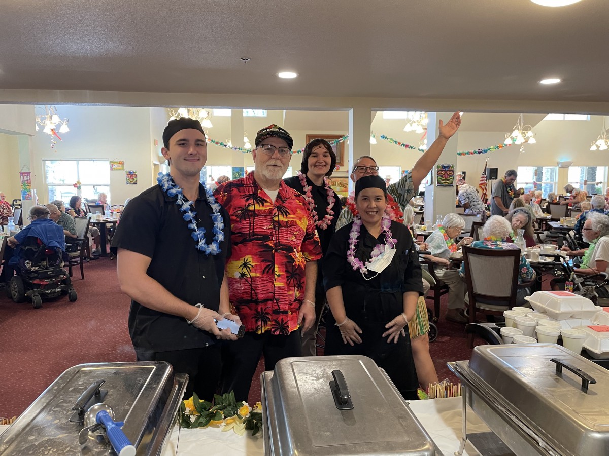 A group of people in casual attire gathered at a buffet event, celebrating with leis.